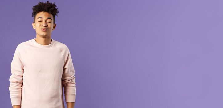 Portrait of cute and silly, young hispanic trying to kiss girl after date for the first time, leaning with folded lips and closed eyes towards her, making funny smile, standing purple background.