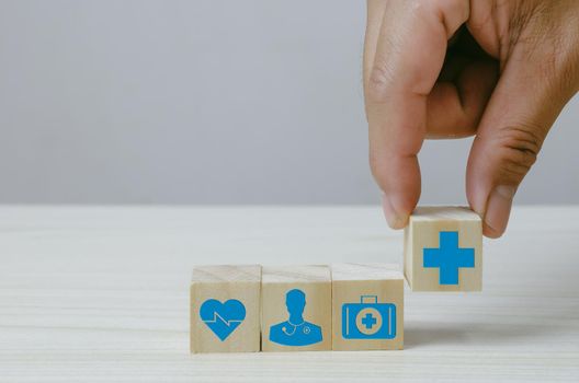 Hand holding wooden cubes block with insurance health car medical symbol on background and copy space.