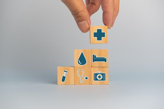 Hand holding wooden cubes block with insurance health car medical symbol on background and copy space.