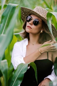 Portrait of young stylish woman in green jungle. Girl in straw hat and sunglasses, linen clothes. Lady looks happy and healthy, she smiles. High quality photo