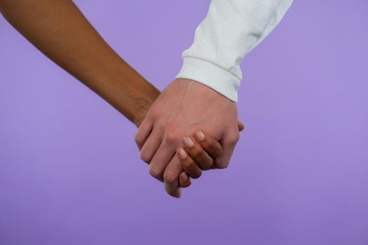 Hands of mixed race woman and white man. Interracial friendship, anti-racism, fraternity. Agreement, cooperation concept on purple background