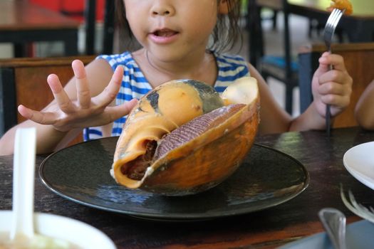 Cute Asian little girl having lunch in a restaurant. Sea food. edible clams. Summer vacation sea trip with family