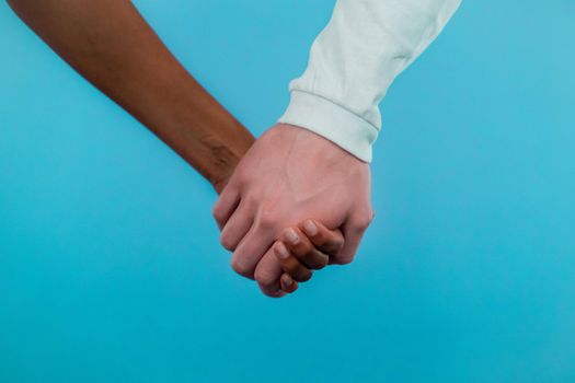 Hands of mixed race woman and white man. Interracial friendship, anti-racism, fraternity. Agreement, cooperation concept on blue background.