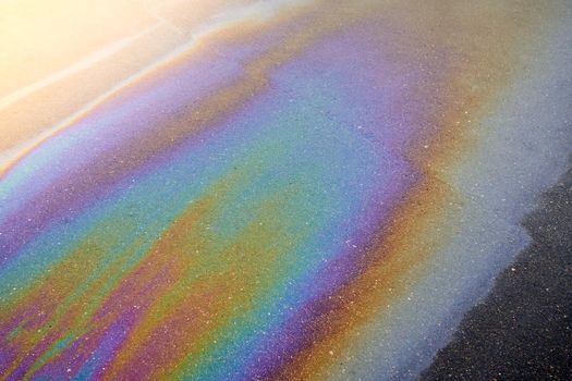 Oil stain on the asphalt, rainbow-shaped colored gasoline stains on an asphalt road as a texture or background