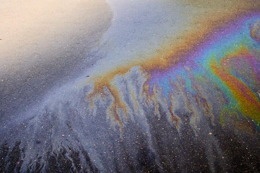 Oil stain on the asphalt, rainbow-shaped colored gasoline stains on an asphalt road as a texture or background. Soft focus