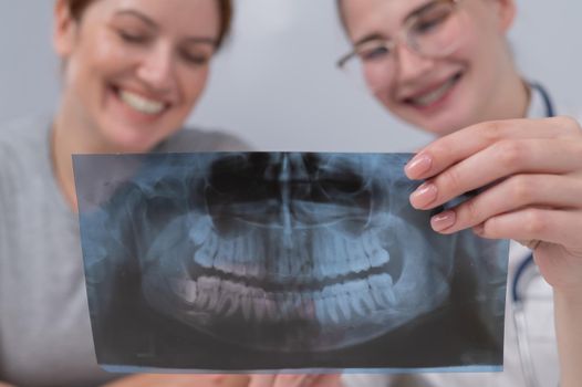 A woman doctor and a patient at the reception are discussing an x-ray of the jaw