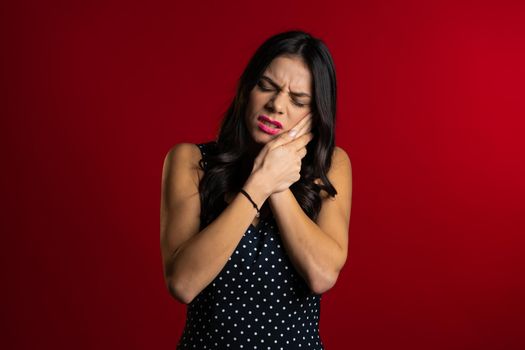Young pretty latin woman with tooth pain on red studio background. Toothache, dental problems, stomatology and medicine concept