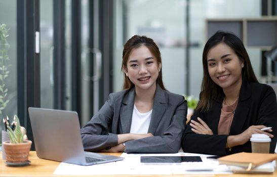 Two young Asian businesswoman discuss investment project working and planning strategy. Business people talking together with laptop computer at office..