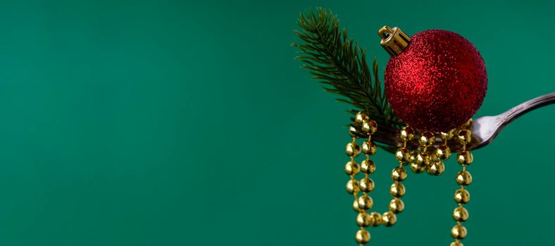 banner with Close up of Christmas decorations on a fork of gold beads, a branch of a Christmas tree and a red Christmas ball on a green background. concept for chinese or oriental new year. copy space