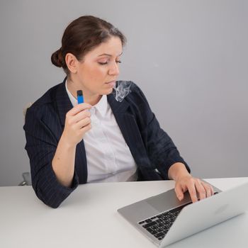 Business woman smoking a disposable vape while sitting at her desk