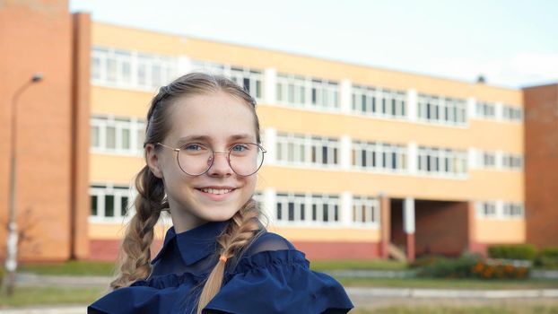 A teenage girl wearing glasses in front of a school