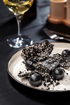 Appetizer with salmon pate, ink cuttlefish, crackers served on white tray over black wooden background. Close-up. Photo for the menu. Molecular gastronomy