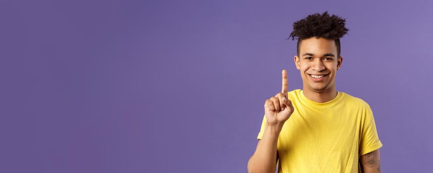 Close-up portrait of funny young teenager, guy picking nose showing index finger and giggle, gagging over his own joke, being nasty and disgusting, standing purple background.