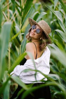 Portrait of young stylish woman in green jungle. Girl in straw hat and sunglasses, linen clothes. Lady looks happy and healthy, she smiles. High quality photo