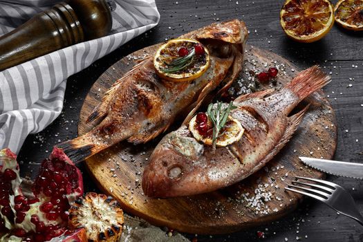 Grilled red mullet on a wooden board with lemon and garnet. Healthy eating concept. Top view. Still life. Flat lay