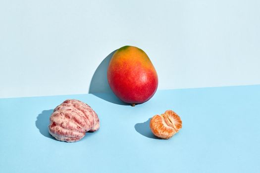 Composition of fresh fruits, mango and mandarin, half of peeled mandarin and mango on blue background. Mock up, two-colored pastel