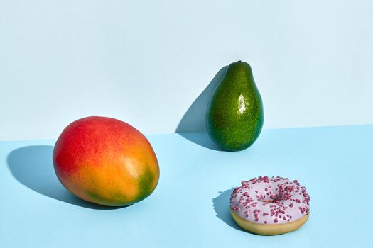 Composition of fresh fruits and sweets, donut mango and avocado on blue background. Mock up, two-colored pastel