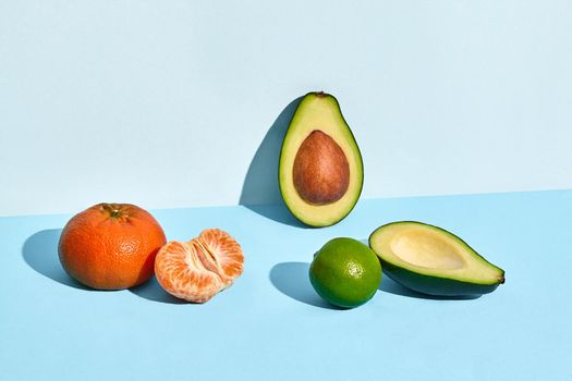 Composition of fresh fruits, mandarin, lime and two halfs of cutted avocado on blue background. Mock up, two-colored pastel