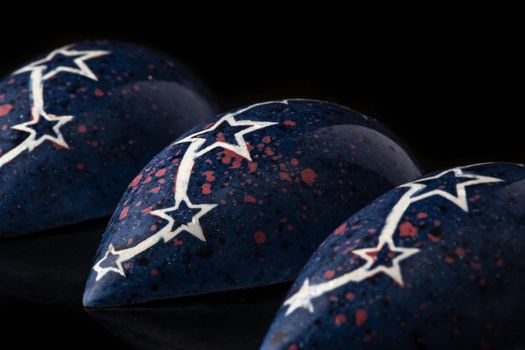 Dark blue luxury handmade chocolate candies with white stars on black background. Exclusive handcrafted bonbon. Product concept for chocolatier