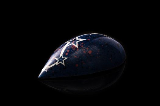 Dark blue luxury handmade chocolate candy with white stars on black background. Exclusive handcrafted bonbon. Product concept for chocolatier