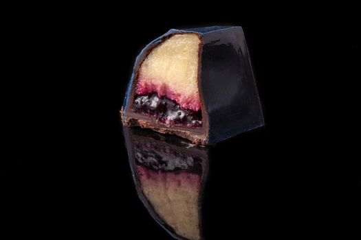 Cut luxury handmade candy with chocolate and red confiture filling on black background. Exclusive handcrafted bonbon