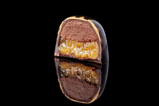 Cut luxury handmade candy with chocolate and yellow confiture filling on black background. Exclusive handcrafted bonbon