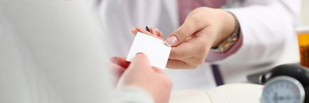 Female doctor hands over white business card to patient. Attending physician choice concept