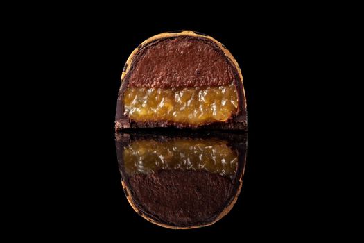Cut luxury handmade candy with chocolate and yellow confiture filling on black background. Exclusive handcrafted bonbon