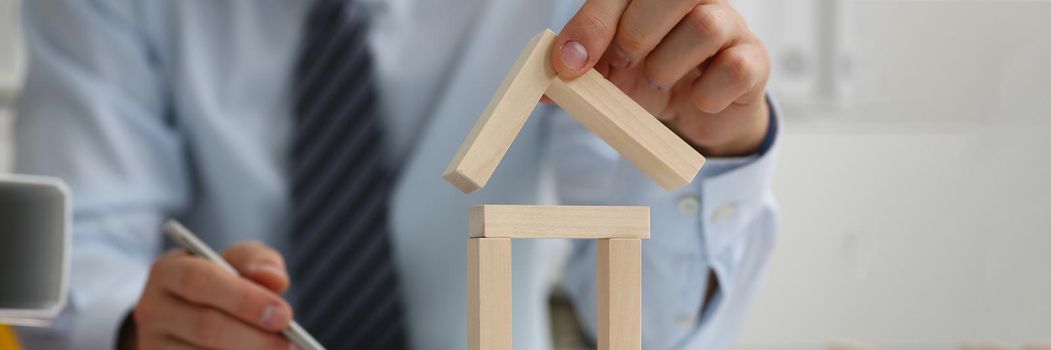 Man hand puts roof on model of house. Real estate construction and renovation concept