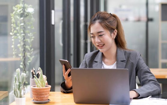 Asian businesswoman in formal suit in office happy and cheerful during using smartphone and working.