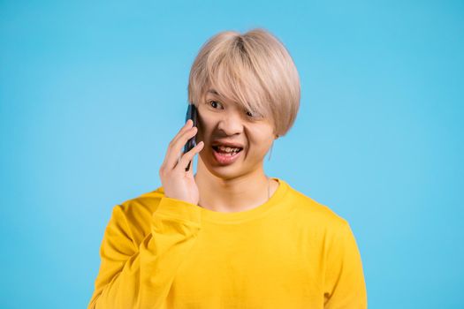 Young angry asian man screaming down his mobile phone. Stressed and depressed man on blue background