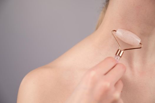 Close-up portrait of a woman using a quartz roller massager for an alternative fight against wrinkles on her neck. Smoothing of the rings of venus