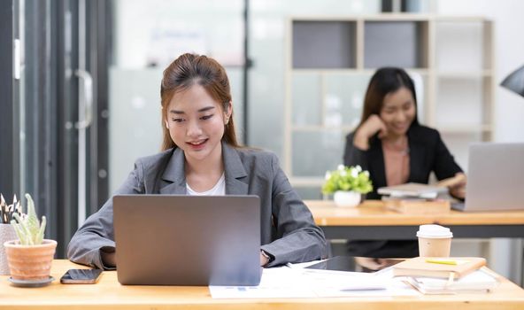 Two business women are working on a notebook computer, holding a pen and looking at the screen in office..