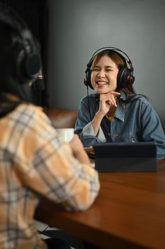 Smiling young woman radio host interviewing guest in studio while recording live podcast in studio.