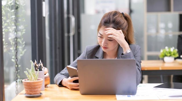 serious young Asian businesswoman at her office desk dealing with a smartphone problem or receiving a complaint email from her boss