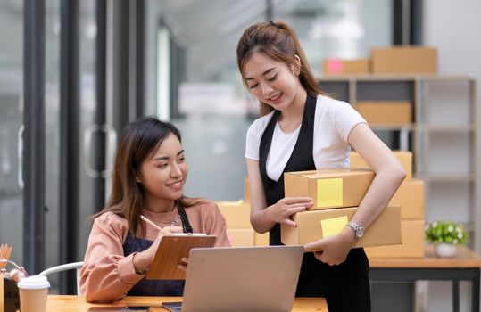 Startup small business owner working with computer at workplace. Freelance two woman seller check product order. Packing goods for delivery to customer. Online selling. E-commerce. Online Shopping.