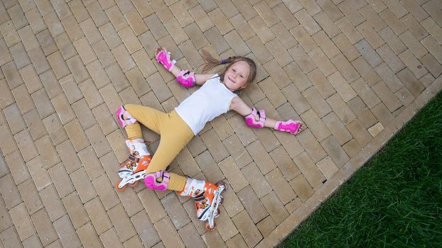 Little girl learns to roller skate and falls. View from above.