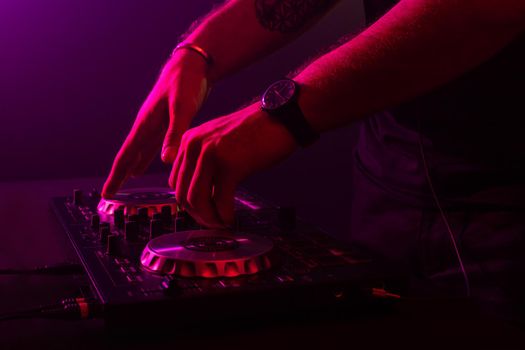 Dj mixing on turntables with color light effects. Soft focus on hand. Close-up. Fun, youth, entertainment and fest concept