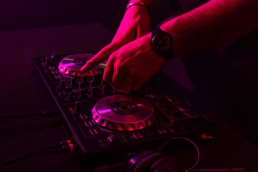 Dj mixing on turntables with color light effects. Soft focus on hand. Close-up. Fun, youth, entertainment and fest concept