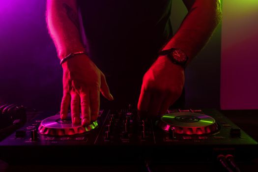 Dj mixing on turntables with color light effects. Soft focus on hand. Close-up. Fun, youth, entertainment and fest concept