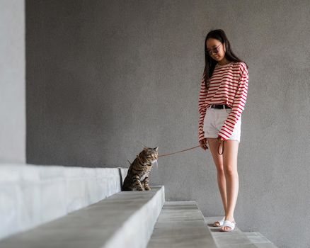 Woman walking with a cat on a leash outdoors in summer