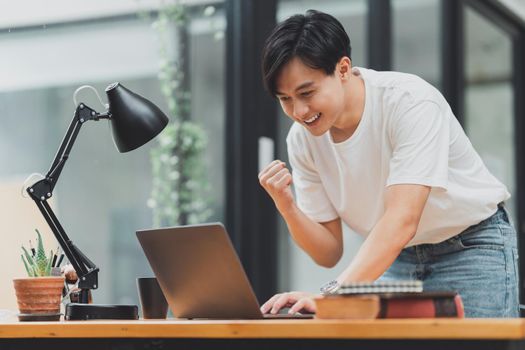 Happy Asian man using laptop computer while have a good news working at office.