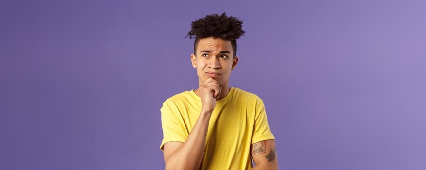 Close-up portrait of indecisive, puzzled attractive young man have problems, lacking idea, thinking, look away frowning and grimacing troubled, standing thoughtful purple background.