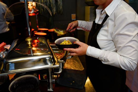 Black bowl with noodles served at a party by a waiter with a black kitchen apron
