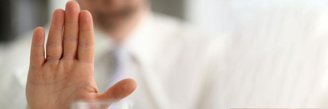 Male hand shows a negative gesture to glass beaker. Refusal of spicy alcoholic drinks concept