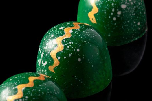 Luxury handmade chocolate candies on black background. Green candies with multicolored drops. Exclusive handcrafted bonbon. Product concept for chocolatier. Close-up
