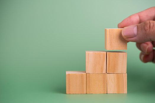 Hand holding wood cube block blank on green background.