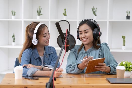 Smile two asian young woman, man radio hosts in headphones, microphone while talk, conversation, recording podcast in broadcasting at studio together. Technology of making record audio concept..