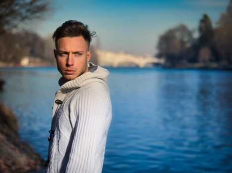 One handsome young man in urban setting in European city, Turin in Italy by the river Po, in cold winter day
