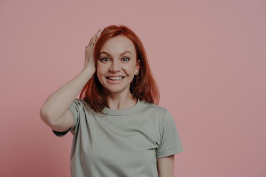 Portrait of excited amazed redhead ginger girl touching head with surprised facial expression, standing astonished isolated over pink background, impressed female with open mouth feeling wondered